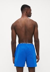 Sinised ujumispüksid, mis on valmistatud kergetest kangast, elastse vöökohtaga, millel on "JACK & JONES" brändimine ja küljetasku.