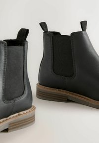 Schwarze Lederstiefeletten mit elastischen Seitenpaneelen, strukturiertem Finish und kleinen Schlaufen; braune, gestapelte Absätze mit subtilen Streifen.