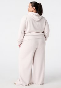 Lichtbeige loungewear-outfit bestaande uit een textuur, oversized hoodie met een capuchon en rechte broek met wijde pijpen. Zacht, comfortabel materiaal met een casual pasvorm.