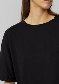 Czarny t-shirt z krótkim rękawem, wykonany z miękkiej bawełny, z okrągłym dekoltem i lekko marszczonymi rękawami dla swobodnego dopasowania.