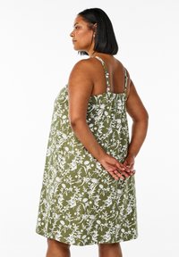 Oljčno zelena poletna obleka z rožnatim vzorcem, tanka naramnica, sproščen kroj in nabran hrbtni del z belimi botaničnimi motivi.