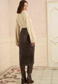 Pulover bej cu dungi și mâneci largi, asortat cu o fustă din piele maro închis, foarte ajustată, cu un model texturat, și cizme maro cu toc înalt.