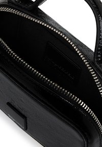 Czarna skórzana torba o teksturowanej powierzchni z otwartym srebrnym zamkiem, ukazująca czarne wnętrze z materiału i małą metalową płytkę z logo z przodu.