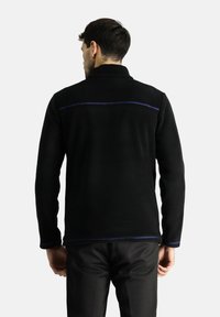 Chaqueta de forro polar negra con cuello alto, detalles de costura azul en la parte posterior y silueta ajustada. Textura suave con mangas largas.