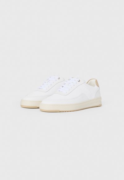 Et par hvite lavtoppsneakers med beige detaljer og hvite lisser, vist mot en lys grå bakgrunn.