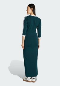 Tyrkysové šaty s tromi štvrtinovými rukávmi, bielym golierom a manžetami, s čiernymi prúžkami na rukávoch, nosené s bielymi teniskami.