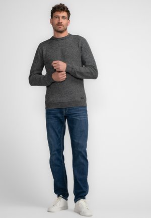 Donkergrijze gebreide trui met een ronde halslijn, lange mouwen en een geribbeld zoom, gecombineerd met blauwe jeans en witte sneakers.