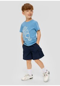 Blauwe katoenen T-shirt met een witte haai graphic, gedragen met marineblauwe cargoshorts. Compleet met witte sneakers en crewlengte sokken.