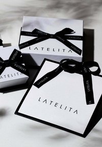 Gift boxes with a black and white theme. The largest has a black ribbon and a logo, while smaller boxes are plain white with black ribbons.