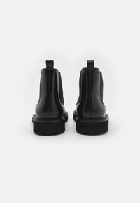 Mustad musta nahast Chelsea saapad, millel on elastsed külgpaneelid, ümarad varbad ja kummised tallad. Omab tagapool tõmblukke, et oleks lihtne jalga panna.