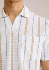 Camisa de manga corta con cuello en una tela texturizada blanca con rayas en azul claro, beige y blanco. Incluye un bolsillo en el pecho.