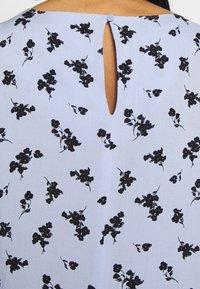 Světle modré šaty s černým květinovým vzorem, s výstřihem na zádech ve tvaru klíčové dírky a knoflíkovým detailem. Měkká textura látky.