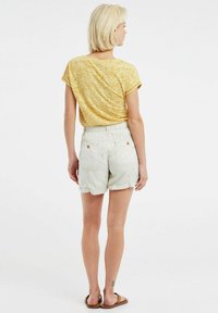 Top giallo a maniche corte con texture, abbinato a pantaloni beige chiaro con tasche e orlo arrotolato. Calzature casual completano il look.