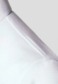 Szczegół kołnierza białej koszuli, wykonany z gładkiej bawełny, z precyzyjnymi szwami i usztywnionym kształtem oraz czystymi krawędziami.