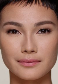 Close-up of a face with smooth, light brown skin, straight dark hair, natural makeup featuring soft pink lips and full eyebrows.