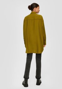 Olijfgroene oversized shirt met een kraag, lange mouwen en knopen. Gecombineerd met donkergrijze opgerolde broeken en zwarte platformlaarzen.