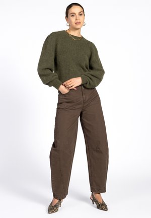 Groene donzige trui met pofmouwen, gecombineerd met een bruine wijdvallende broek en schoenen met luipaardprint. Eenvoudige ketting als accent.