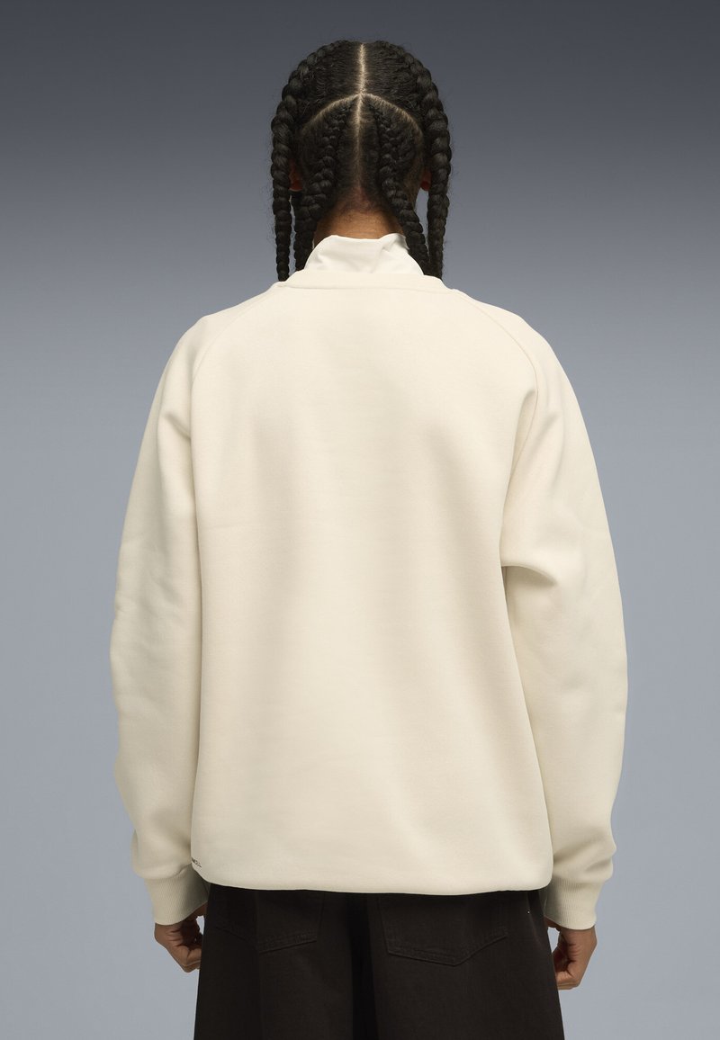 Felpa di colore crema con vestibilità rilassata, polsini a coste e colletto alto, che mostra una texture liscia e morbida senza marchi visibili.