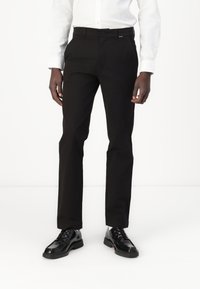 Pantaloni negri dintr-un material neted, croi ajustat, cu față plată și bucle pentru curea. Asortați cu pantofi eleganți negri, lucioși.