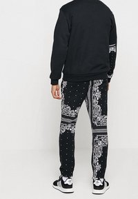 Černá mikina s kulatým výstřihem. Černé kalhoty s bílým paisley vzorem a puntíky, doplněné černobílými teniskami.