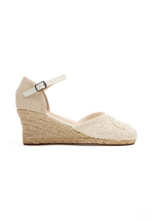 Alpargata beige con cuña, tacón de cuerda trenzada, puntera bordada y correa ajustable blanca en el tobillo con hebilla plateada.