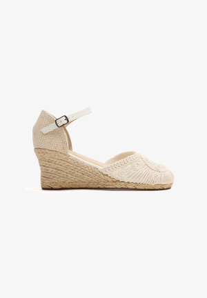 Alpargata beige con cuña, tacón de cuerda trenzada, puntera bordada y correa ajustable blanca en el tobillo con hebilla plateada.