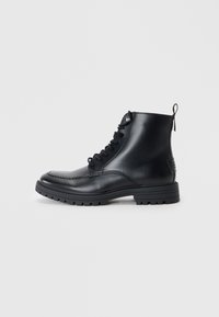 Botas de tobillo de cuero negro con puntera redonda, cordones en la parte delantera y detalles de costura. Cuentan con una pestaña en la parte trasera y una suela de goma texturizada.