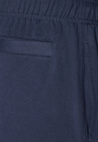 Dunkelblaue Baumwoll-Sweatpants mit einem elastischen Bund, ausgestattet mit einer einzelnen Gesäßtasche und glatter Textur. Minimalistisches Design.