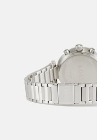 Sølv klokke med en metall lenke armbånd, som har et rundt hus og tre trykkere. Baksiden viser logo og detaljer om vannmotstand.