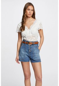 Haut en dentelle blanche à manches courtes, décolleté en V, associé à un short en denim bleu taille haute avec une ceinture brune et une fermeture à bouton.