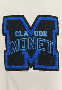 Černý a modrý vyšívaný design s velkým písmenem "M" a jménem "CLAUDE MONET" na krémově zbarveném pozadí.