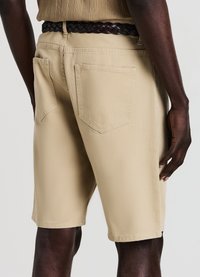 Shorts in denim beige con una texture liscia, tasche posteriori e taglio dritto; abbinati a una cintura intrecciata scura.