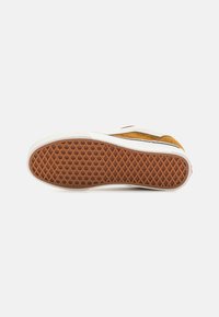 Brun og hvit sneakersåle med en teksturert gummibunn som har et honningkombinasjonsmønster, omkranset av en glatt hvit mellomsåle.