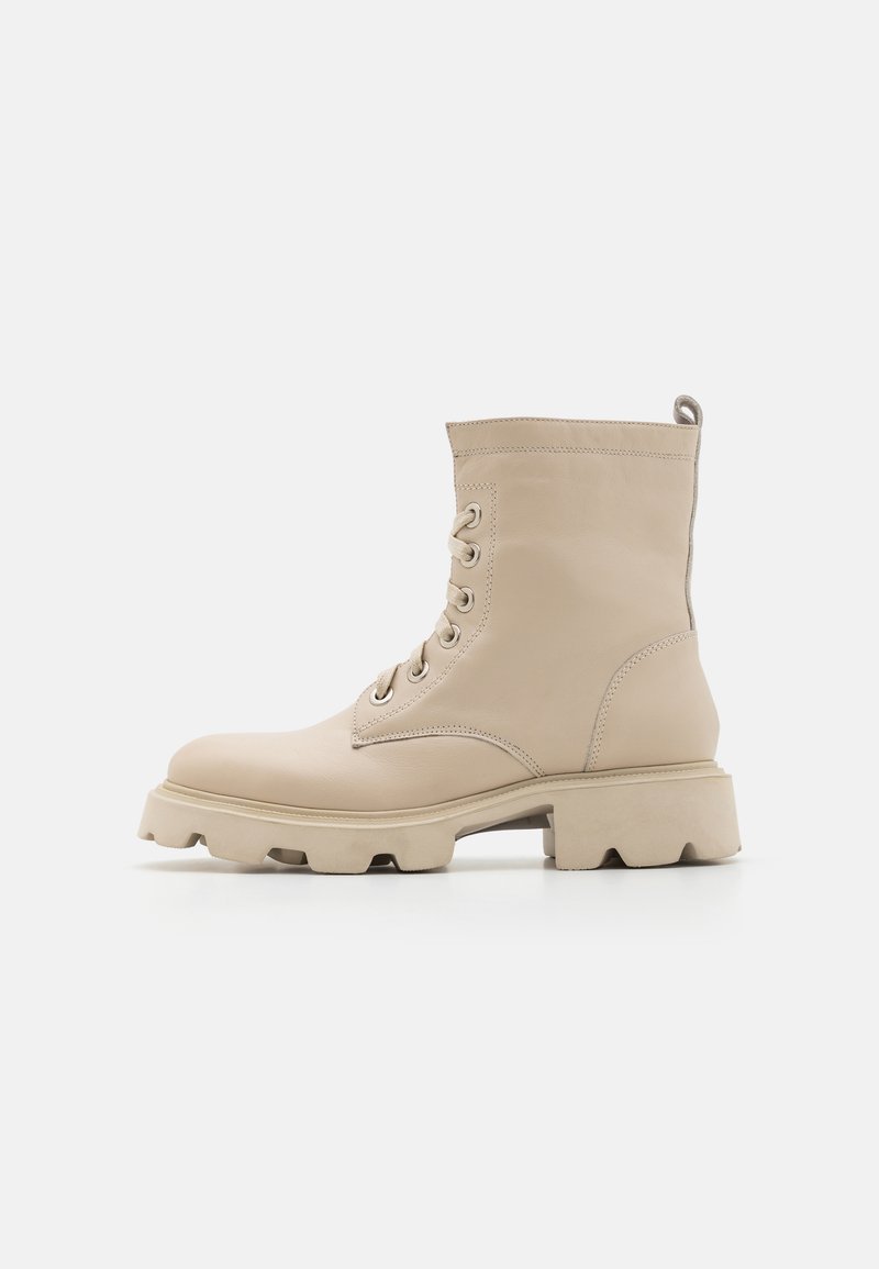 Stivaletto in pelle beige alla caviglia con punta tonda, allacciatura frontale e suola in gomma spessa con un design a bordi frastagliati.