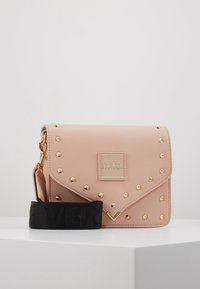 Blush pink leather crossbody bag with gold studs, magnetic flap closure, and a black fabric strap featuring embossed branding.