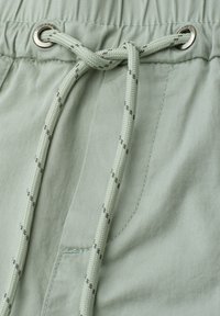 Shorts en tissu vert clair avec une ceinture élastique et un cordon noué passant à travers des œillets métalliques.