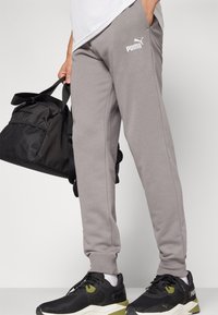 Grijze joggerbroeken van zacht materiaal, met een tapered fit en elastische boorden. Een wit Puma-logo is weergegeven op de dij.