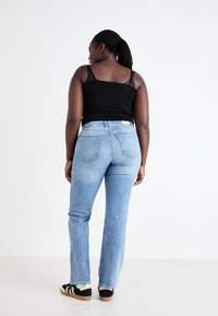 Calças de ganga azul clara com corte reto, cinco bolsos e detalhes de costura discretos. Usadas com uma camiseta preta sem mangas e ténis pretos.