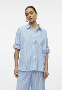Camicia button-up a righe blu e bianche con una vestibilità rilassata, maniche corte arrotolate e colletto. Il tessuto sembra leggero e traspirante.