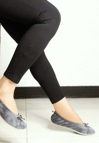 Ballerines en velours gris avec un bout arrondi, une petite attention de nœud, portées avec des leggings noirs, positionnées pour montrer le design de la chaussure.