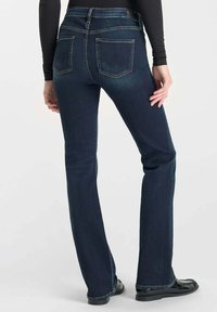 Jeans en denim bleu foncé à jambe évasée, avec des coutures discrètes sur les poches arrière et une taille haute. Pas d'embellissements visibles.