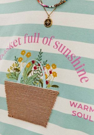 Jasnoniebieska bluzka w paski w kremowym kolorze z kwiatowym wzorem i napisem. Posiada teksturowany, pleciony detal kieszeni z przodu.