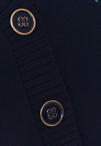 Deux boutons bleu foncé aux bords dorés fixés sur un tissu tricoté bleu foncé, mettant en valeur la texture et les détails des boutons.