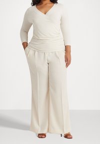 Beige långärmad omslagstopp i kombination med lösa, högmidjade byxor. Mjuk tyg med subtil drapering; sandaler med små klackar.