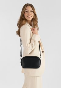 Borsa a tracolla in pelle nera con superficie testurizzata, forma ovale e tracolla regolabile. Chiusura con cerniera e dettagli in metallo argentato.