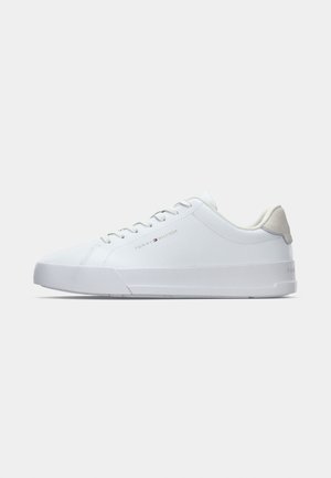 White low-top sneaker with lace-up front, gray suede heel patch, and "Tommy Hilfiger" logo on the side.