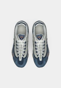 New Balance sneakers featuring a mix of navy blue and gray mesh and synthetic material, with a textured sole and contrasting white laces.