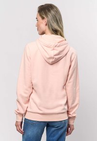 Svetlo roza pulover s kapuco, dolgimi rokavi, rebrastimi manšetami in robom. Ima žep kenguru, mehko teksturo in sproščen kroj.