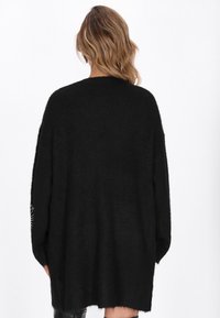 Svart oversized tröja, mjukt stickat material, ribbat halsringning och muddar, något längre bakstycke och diskret detaljering på ärmarna.