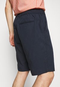 Man som bär marinblå shorts och en korall- och vitrandig skjorta, visad från baksidan vid lågnivå.